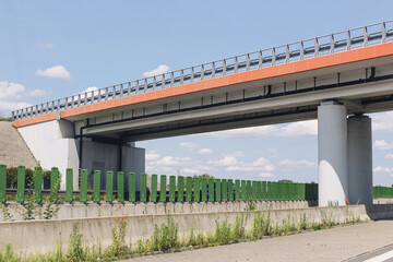 Fototapeta premium Modern road overpass bridge. Concrete highway infrastructure with sound barriers. Urban transport construction detail. Clear blue sky background. Civil engineering scene. Roadside pedestrian sidewalk.