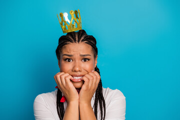 Young woman with braided hair wearing a crown expressing anxiety against a vibrant blue backdrop