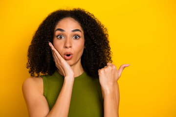 Surprised young woman pointing to the side with expressive emotion, wearing a green top against a...