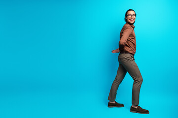 Smiling young businessman walking confidently against a vibrant turquoise background, emphasizing...