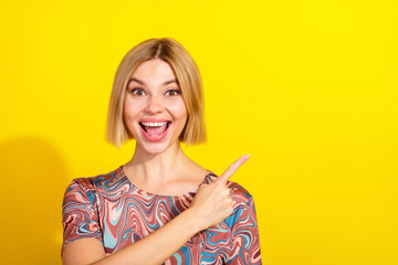 Cheerful young woman pointing upward against a vibrant yellow backdrop in stylish attire with a...
