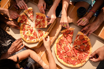 Group of friends sharing pizza outdoors on a sunny day, celebrating togetherness and enjoying...