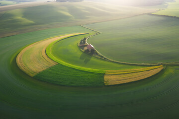 Scenic aerial view showcases rolling green agricultural fields with a charming farmhouse nestled among trees in a vibrant landscape.