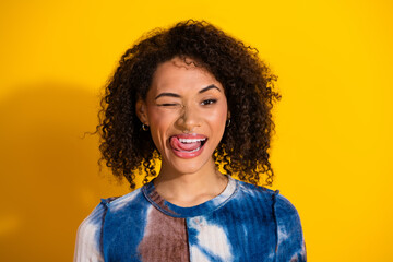 Joyful young woman winking playfully while posing against a vibrant yellow background in a stylish...