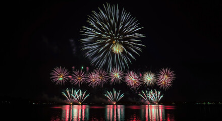 Spectacular fireworks display over water at night with colorful reflections on lake surface. Vibrant pyrotechnic show against dark sky. Festive celebration event with synchronized light performance