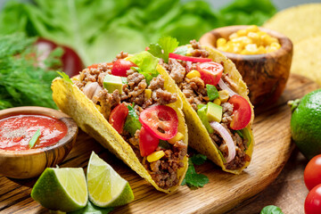 Mexican meat tacos or beef stuffed tortillas and lime slices near them on wooden serving board.