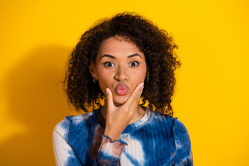 Fashionable young woman with curly hair in a stylish printed shirt posing against a vibrant yellow...