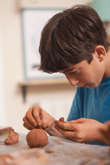 Teen boy sculpting clay with focus during creative activity at home