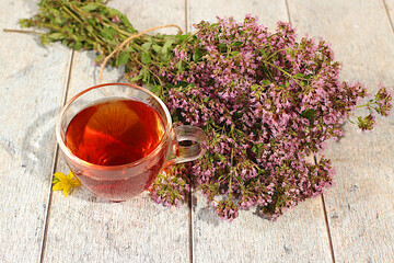 Medicinal herbal tea or oregano infusion in a glass with flowers, alternative folk medicine concept, green pharmacy advertisement, collection of useful herbs for treatment according to folk recipes,