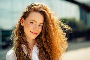Confident young businesswoman with curly red hair enjoying an outdoor urban environment in daylight