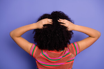 Charming young woman with curly hair posing against a vibrant violet background in a trendy...