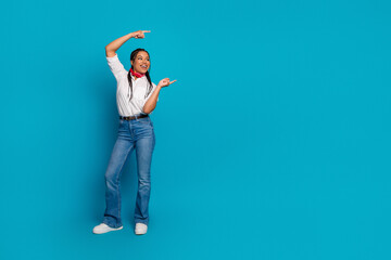 Energetic young woman posing confidently on blue background wearing casual fashion outfit with...