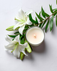 Elegant white lilies with green leaves and scented candle, spa-like composition in bright sunlight