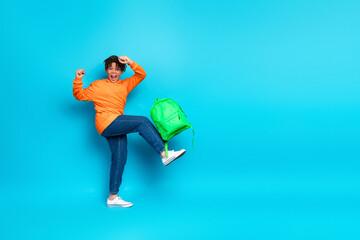 Excited boy with a green backpack posing energetically in casual orange hoodie against bright blue background