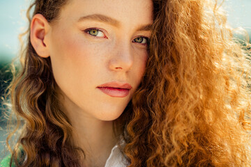 Portrait of a confident young woman outdoors during daytime with natural makeup and red curly hair...