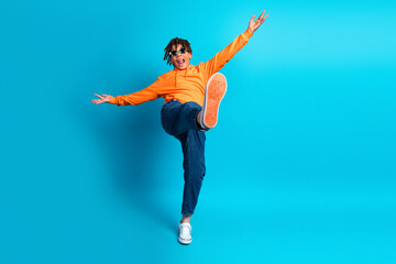 Energetic young boy in orange hoodie makes dynamic pose against bright blue background, showing...
