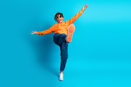 Energetic young boy in orange hoodie makes dynamic pose against bright blue background, showing playful energy and youthful style - Powered by Adobe