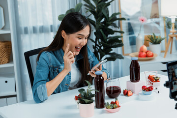 Smiling young beautiful Asian reviewing tasty mixed strawberry and cherry juice detox drinks,...
