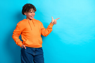 Cheerful young boy in an orange hoodie making a pointing gesture against a vibrant blue background