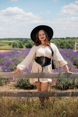 Woman in a white dress and black hat poses in a lavender field on a sunny day during summer