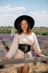 Obraz premium Woman in a white dress and black hat poses in a lavender field on a sunny day during summer