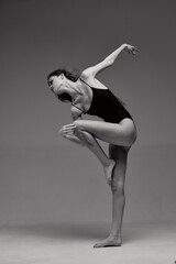 Black and white image of a graceful woman dancer in a leotard performing an elegant contemporary pose against a plain background, showcasing balance and flexibility.