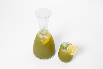Homemade tarragon soda in a glass pitcher and a glass with a lemon slice, isolated on white background
