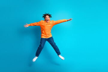 Energetic student jumping in a bright orange hoodie against a vibrant blue background, expressing...