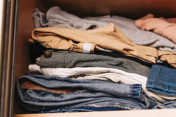 Neatly folded clothes in wooden drawer. Organized stack of pants, shirts and jeans. Casual wardrobe...