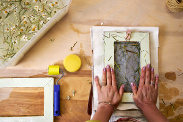 Close-up of hands pressing water out of handmade floral paper with sponge. Final stage of...