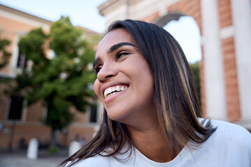 Close-up of a cheerful young latin woman with long brown hair, wearing a white t-shirt, smiling...