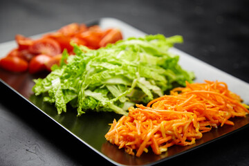 Freshly prepared vegetables including shredded carrots, crisp lettuce, and cherry tomatoes arranged on a black plate, showcasing vibrant colors and healthy eating concepts
