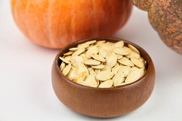Bowl filled with pumpkin seeds sits on a white surface, surrounded by vibrant pumpkins, showcasing the harvest season and natural food elements for culinary inspiration