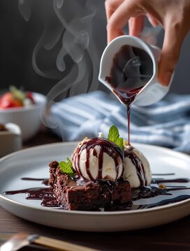 Food photography of a hand pouring chocolate sauce on top of a brownie with ice cream, on a plate against white bacground, with moody lighting, in the style of Unsp