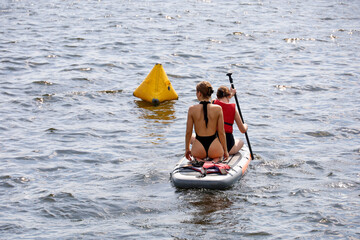 Sup surfing, two girls with paddle sailing on a board in water. Stand up paddle boarding in summer