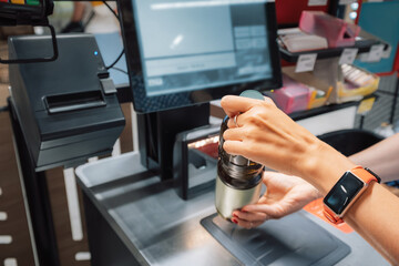 Female cashier scanning groceries at checkout counter in supermarket, using barcode scanner and...