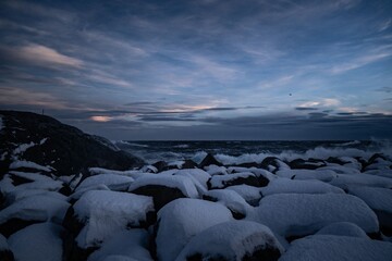 Obraz premium Snow-covered rocks by the sea at dusk.