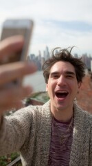 Vertical shot of happy young man having video call on rooftop with distant city in background.
