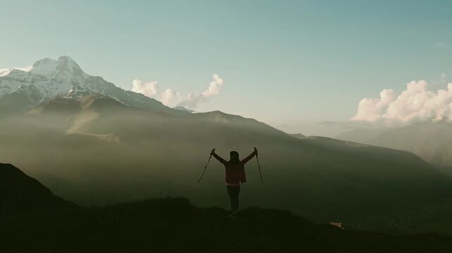 Aerial Cinematic vintage Silhouette of excited woman person celebrating hands up outdoors atop a mountain at sunrise, captured from a low angle. Ideal for an inspirational video theme