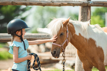 Cute little girl petting a pony in a farm