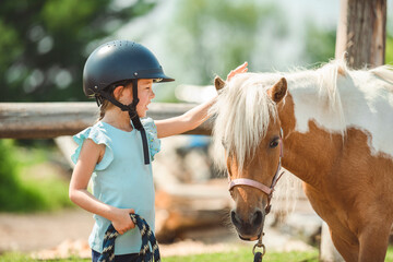 Cute little girl petting a pony in a farm
