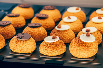 Freshly baked cream puffs topped with white and dark chocolate and nuts, arranged on a tray, creating a tempting display