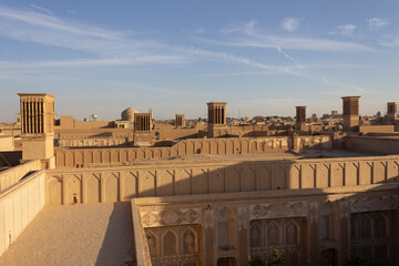 Traditional windcatchers (badgirs) and adobe rooftops in the historic city of Yazd, Iran, under a clear blue sky at sunset.