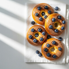 Overhead vibrant shot of golden bagels topped with cinnamon sugar and fresh blueberries on linen napkin. Dappled natural light, copy space on one side copy