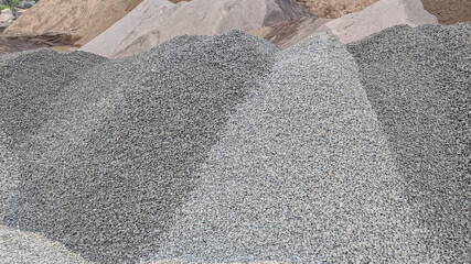 Piles of various grades of crushed stone and sand at a construction material site, showing texture differences used for building, road base, and concrete production.