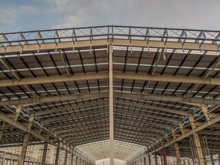 Wide-angle view of an industrial steel structure under construction, showing the metal roof framework and support beams in symmetry during daylight.