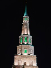 Illuminated tower with green accents stands tall against the night sky in a city of historical significance and architectural beauty