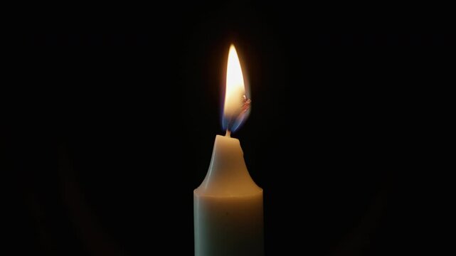 Glowing wax taper standing against shadowed backdrop closeup. Burning candle