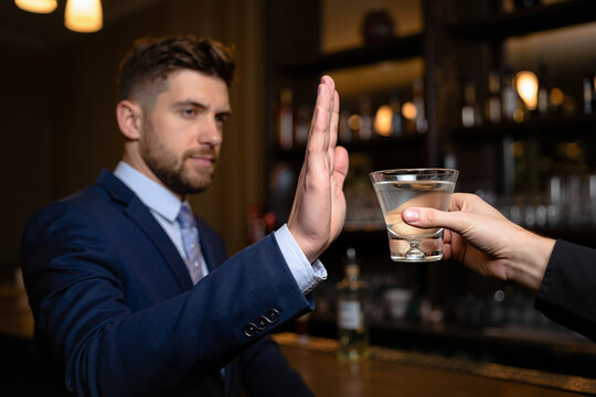 Man refusing a drink while standing at a bar in business attire  