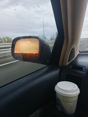 Evening drive with sunset reflections in side mirror and a warm drink on passenger seat